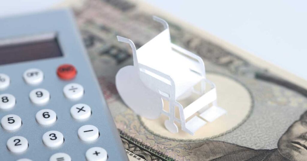 電卓と車椅子の模型、お金の上に置かれた介護費用をイメージした写真