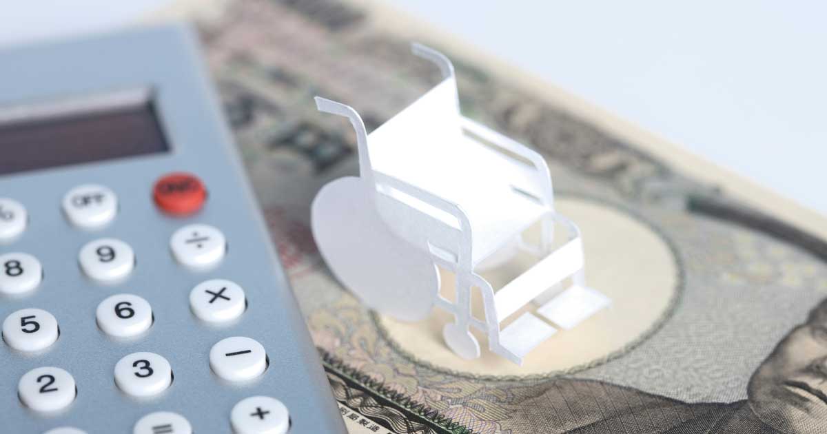 電卓と車椅子の模型、お金の上に置かれた介護費用をイメージした写真