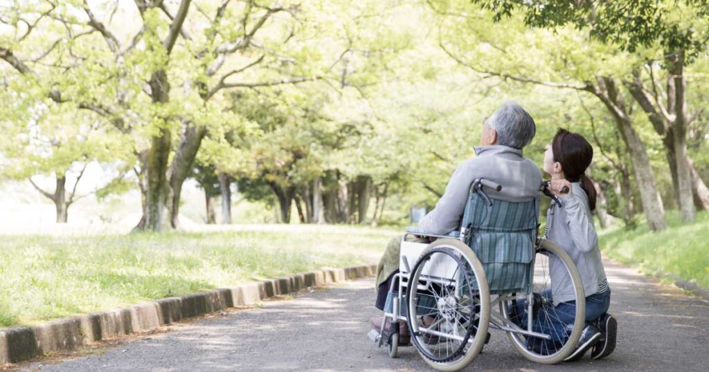 在宅介護で車椅子の高齢者と家族が公園の道を一緒に過ごす様子