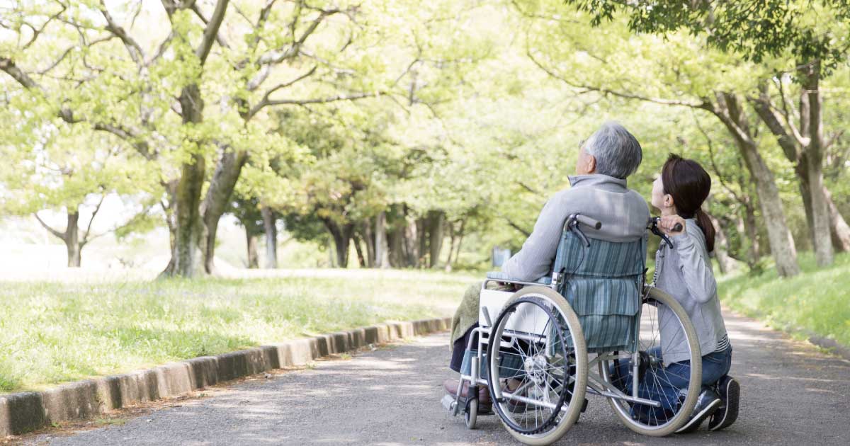 在宅介護で車椅子の高齢者と家族が公園の道を一緒に過ごす様子